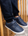Zapatilla escolar barefoot azul marino modelo Dash con doble velcro para kids en uso vista lateral sentado