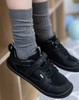Zapatilla escolar barefoot negra modelo Dune con velcro para kids en uso vista lateral parado