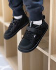 Zapatilla escolar barefoot negra modelo Dune con velcro para kids en uso vista lateral sentado