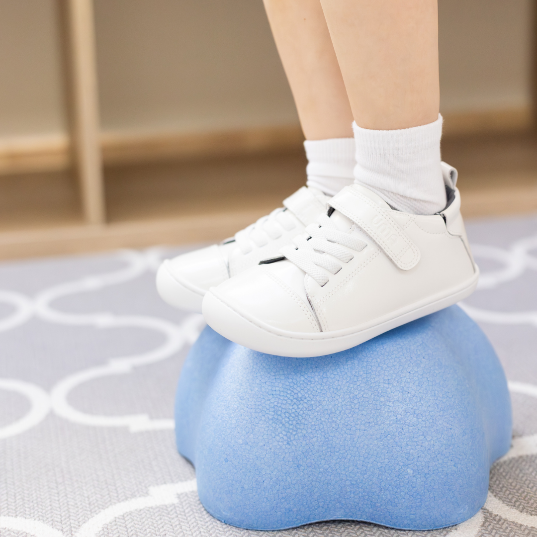 Zapatilla escolar barefoot blanca modelo Cloud con elásticos para toddler en uso sobre superficie sensorial
