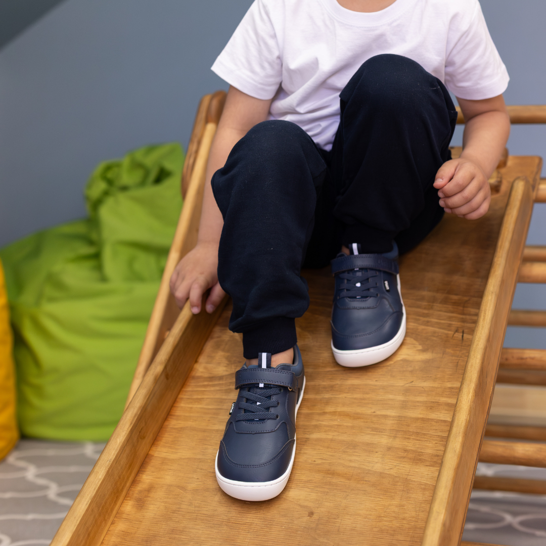 Zapatilla escolar barefoot azul marino modelo Dash con doble velcro para kids en uso vista superior niño sentado
