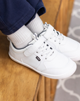 Zapatilla escolar barefoot blanca modelo Dash con doble velcro para toddler en uso lateral calzando
