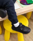 Zapatilla escolar barefoot negra modelo Dash con doble velcro para kids en uso vista lateral
