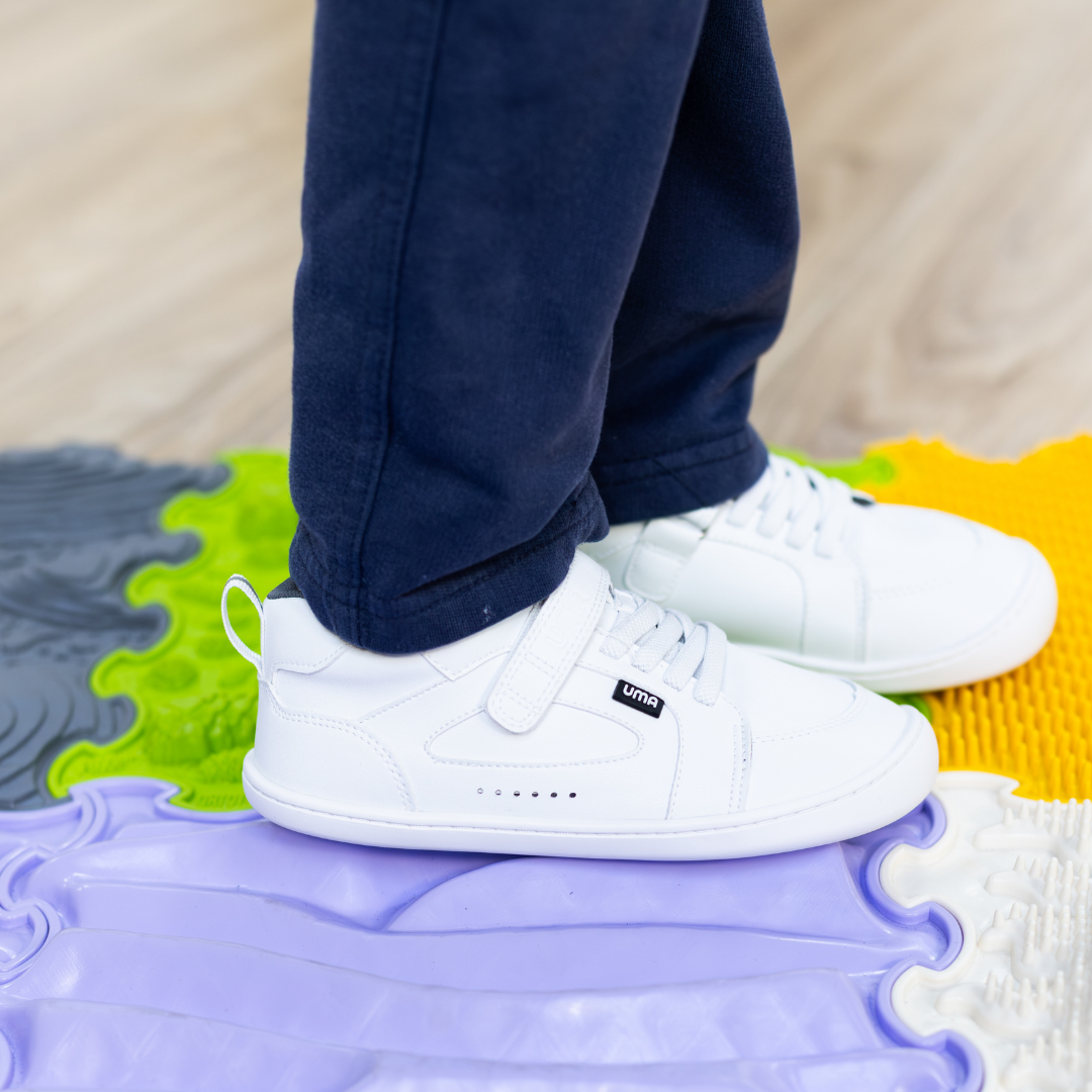 Zapatilla escolar barefoot blanca modelo Dune con velcro para kids en uso sobre superficie sensorial vista lateral
