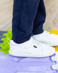 Zapatilla escolar barefoot blanca modelo Dune con velcro para kids en uso sobre superficie sensorial vista lateral
