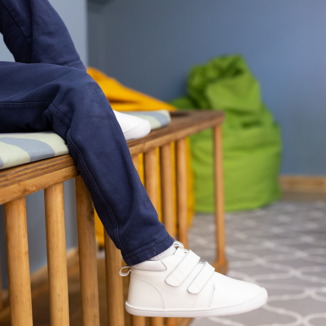Zapatilla escolar barefoot blanca modelo Rain media caña para kids en uso vista lateral sentado