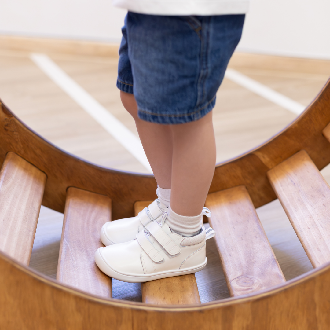Zapatilla escolar barefoot blanca modelo Rain media caña para toddler en uso sobre tabla equilibrio

