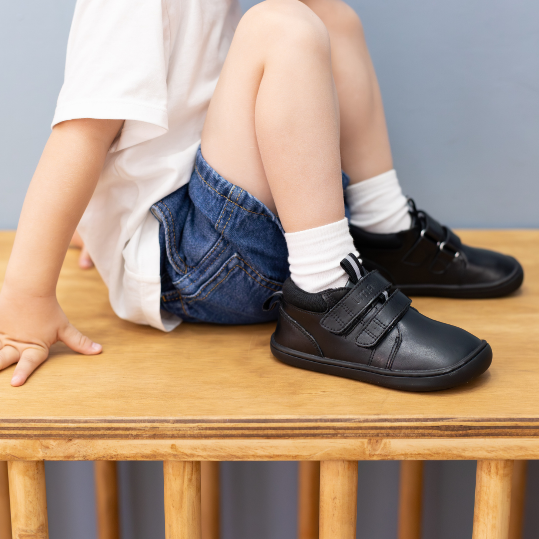 Zapatilla escolar barefoot negra modelo Rain media caña para toddler en uso niño sentado
